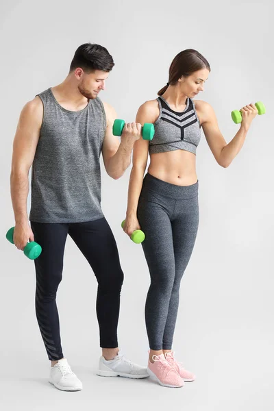 Sporty young couple with dumbbells on light background — Stock Photo, Image