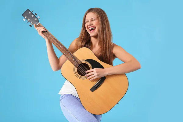 Mooie jonge vrouw met gitaar zingen op kleur achtergrond — Stockfoto