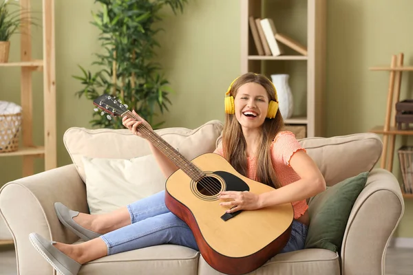 Belle jeune femme avec guitare écoutant de la musique à la maison — Photo