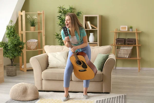 집에서 기타를 치며 노래하는 아름다운 젊은 여자 — 스톡 사진
