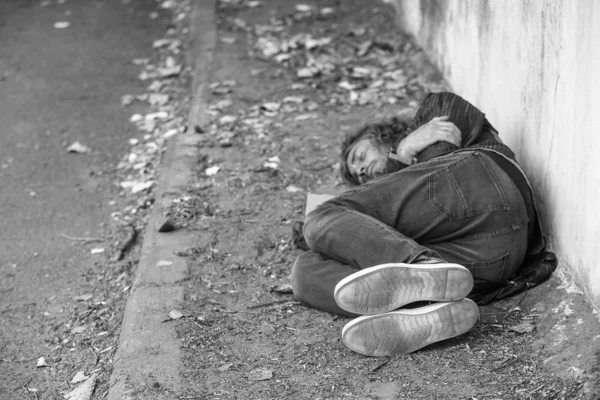 Foto en blanco y negro de un pobre vagabundo durmiendo en el suelo al aire libre —  Fotos de Stock