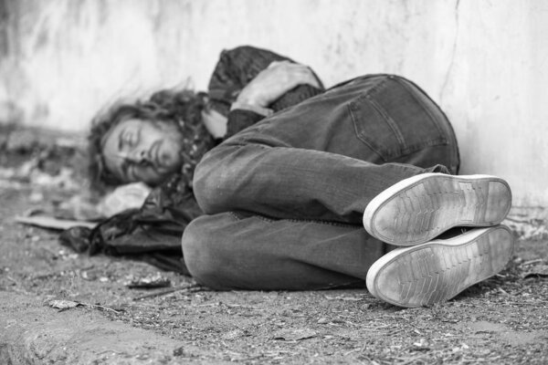 Black and white photo of poor homeless man sleeping on ground outdoors