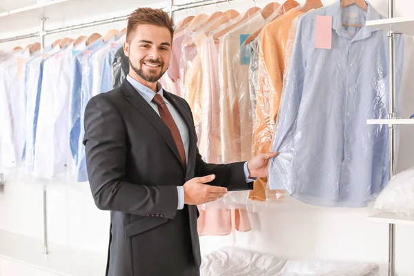 Jonge mannelijke werkster in de buurt van rek met kleren bij de stomerij — Stockfoto