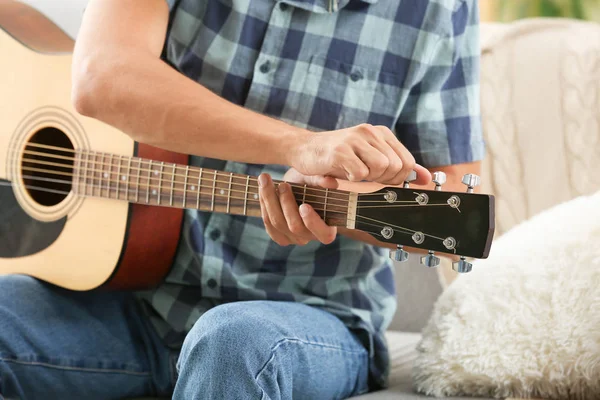 Handsome man tightening guitar strings at home — Stock Photo, Image