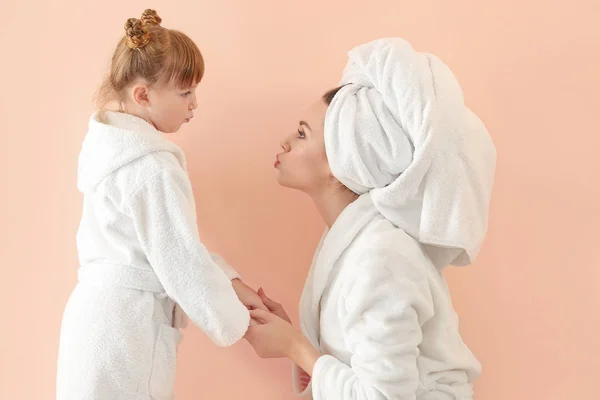 Portrait of happy mother and daughter in bathrobes on color background — Stock Photo, Image