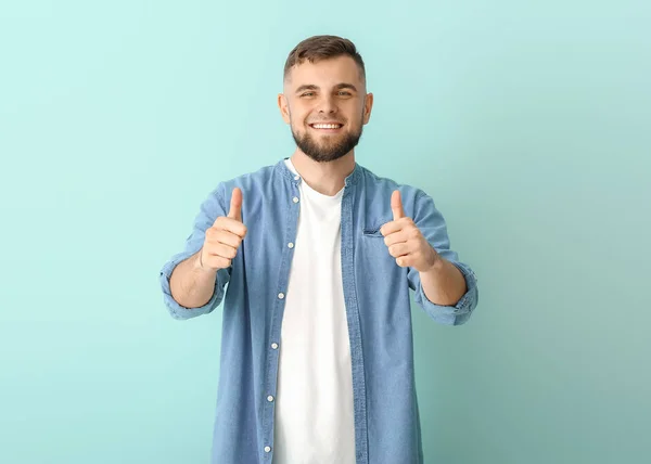 Handsome young man showing thumb-up gesture on color background — Stock Photo, Image