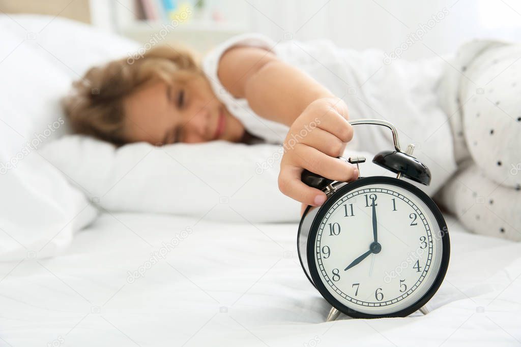 Cute little girl turning off alarm clock in morning