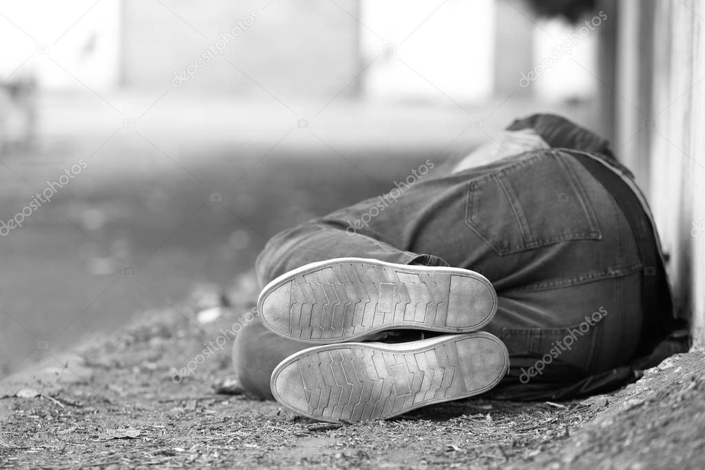 Black and white photo of poor homeless man sleeping on ground outdoors