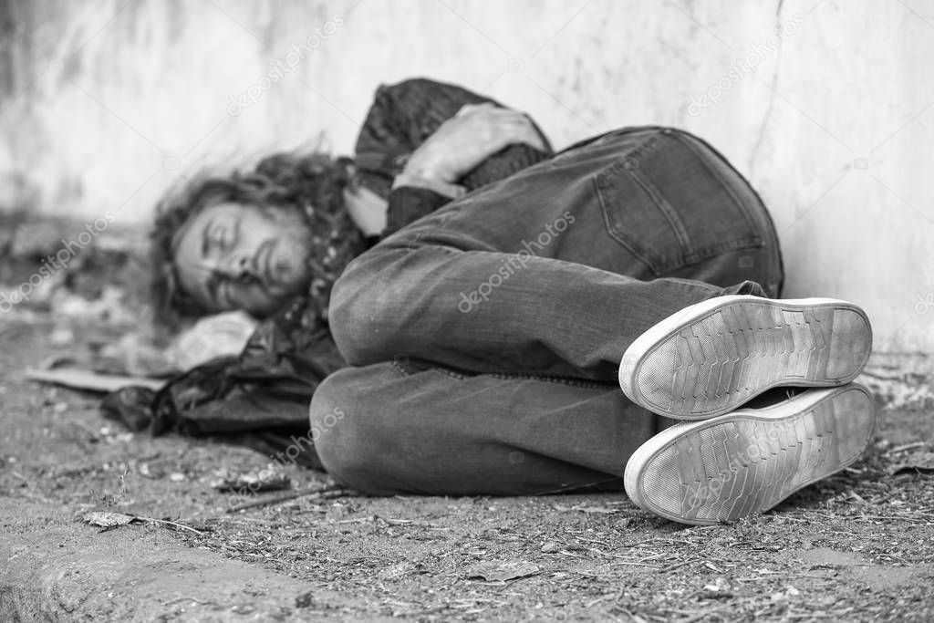 Black and white photo of poor homeless man sleeping on ground outdoors