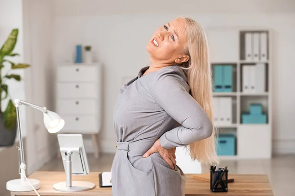 Зрелая женщина страдает от болей в спине в офисе — стоковое фото