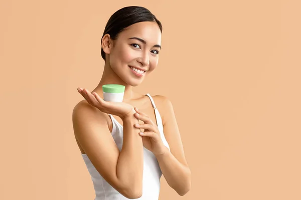 Beautiful Asian woman with jar of cream on color background — Stock Photo, Image