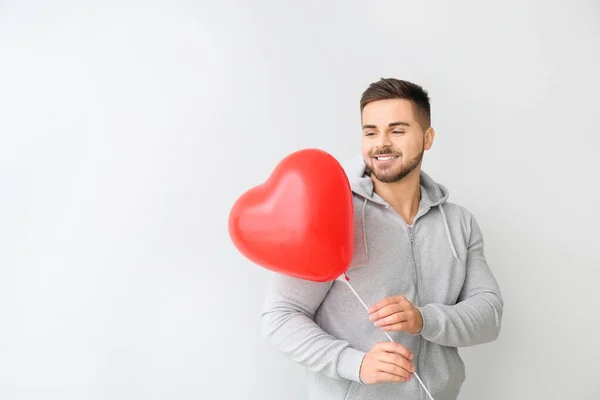 Handsome man with heart-shaped balloon on light background. Valentine's Day celebration — Stock Photo, Image