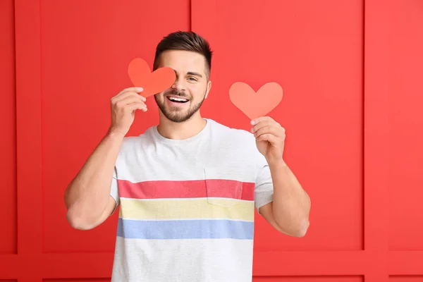 Hombre guapo con corazones rojos sobre fondo de color. Celebración de San Valentín —  Fotos de Stock