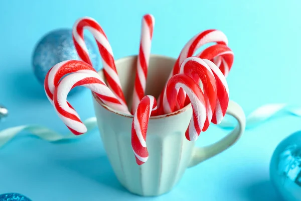Mug with Christmas candy canes and decor on color background — Stock Photo, Image