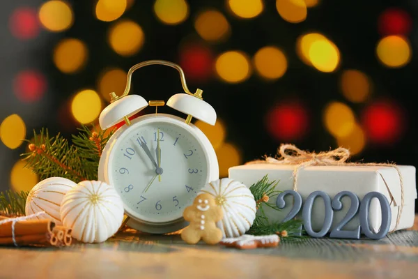 Reloj despertador con decoración navideña y regalo en la mesa contra luces desenfocadas —  Fotos de Stock
