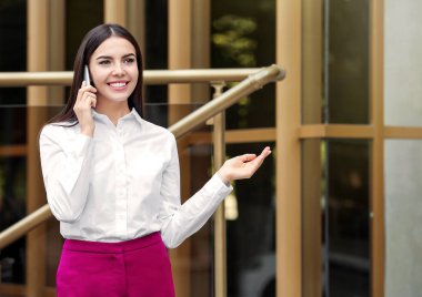 Güzel genç iş kadını dışarıda telefonla konuşuyor.