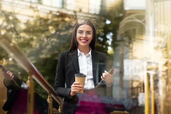 Hermosa joven empresaria con café y tableta al aire libre, vista a través del vidrio — Foto de Stock