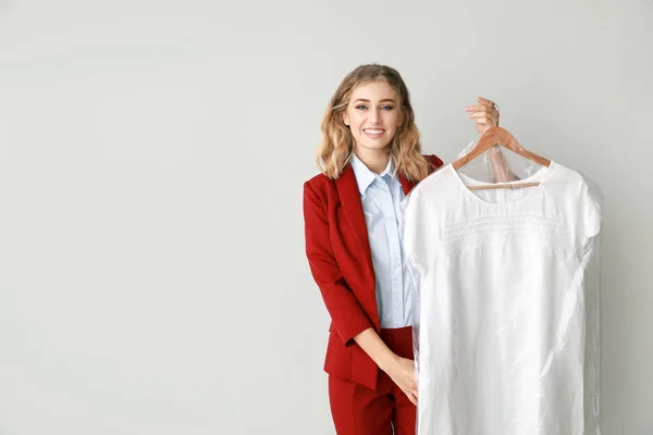 Female worker of modern dry-cleaner with clothes on light background — Stock Photo, Image
