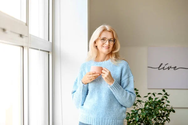 Portrait of beautiful mature woman drinking coffee near window — Stock Photo, Image