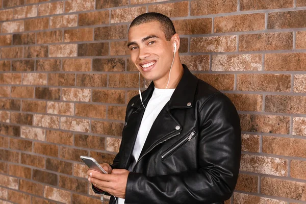 Portrait of handsome young man listening to music near brick wall — Stock Photo, Image