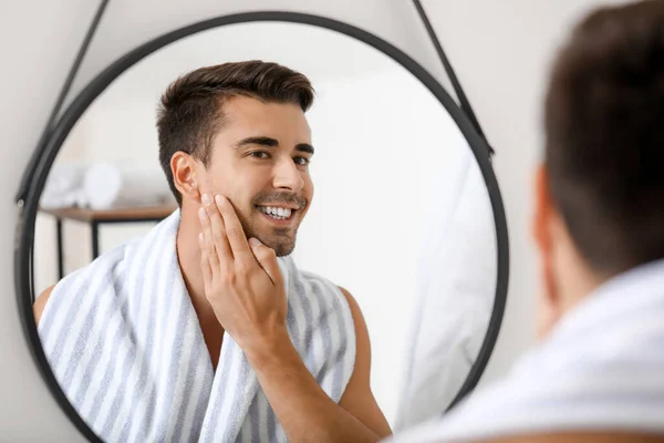 Handsome young man looking in mirror after shaving at home — Stock Photo, Image