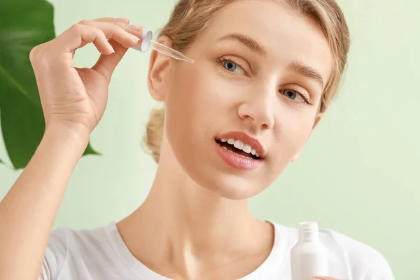 Beautiful young woman with cosmetic product on light background — Stock Photo, Image