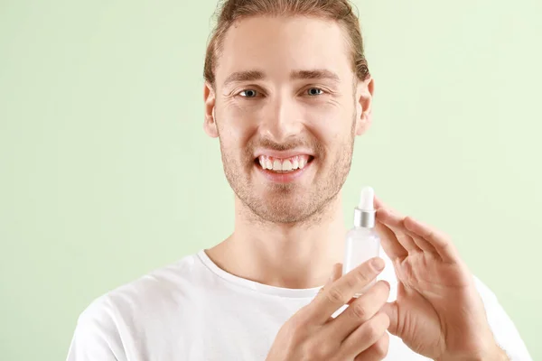 Handsome young man with cosmetic product on light background — Stock Photo, Image