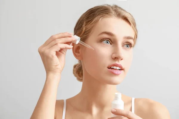 Beautiful young woman with cosmetic product on light background — Stock Photo, Image