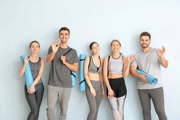 Grupo de pessoas com tapetes de ioga mostrando OK perto da parede de cor — Fotografia de Stock