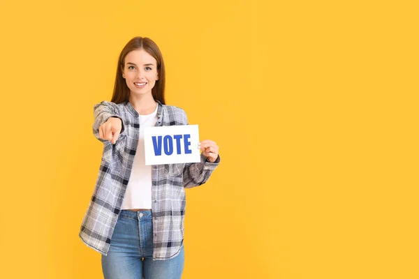 Young woman holding paper with text VOTE on color background — Stock Photo, Image