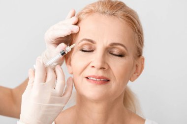 Mature woman receiving anti-aging injection in her face against light background