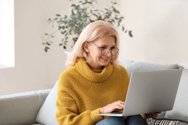 Evde dizüstü bilgisayar kullanan güzel olgun bir kadın.