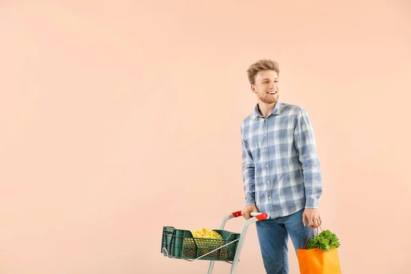 Fiatal férfi bevásárlókosár színes háttér — Stock Fotó