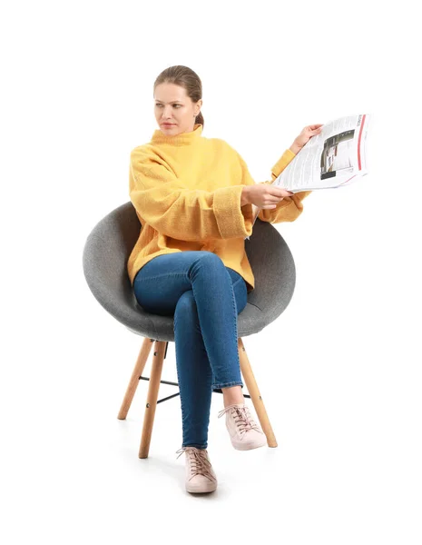 Young woman with newspaper sitting in armchair against white background — Stock Photo, Image