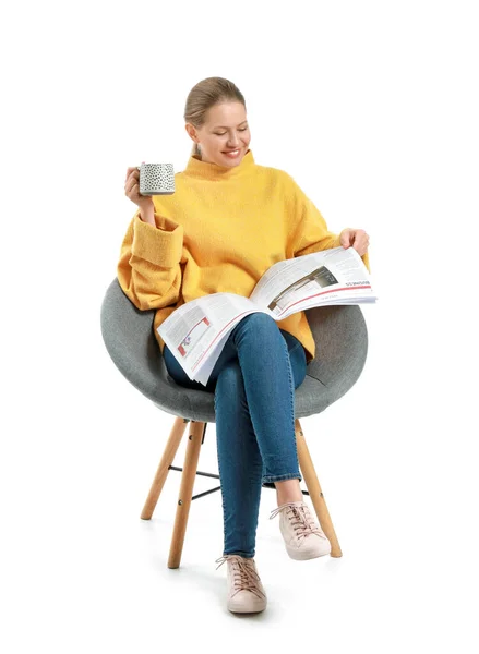 Young woman with newspaper and cup of coffee sitting in armchair against white background — Stock Photo, Image