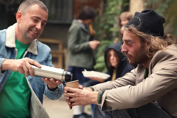 Volunteer giving drink to homeless man outdoors — Stock Photo, Image