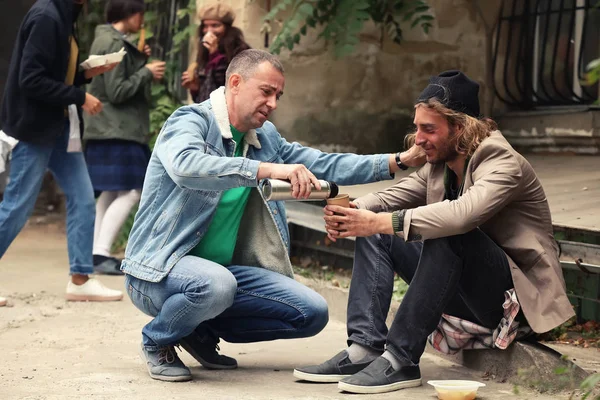 Vrijwilliger drinken geven aan dakloze man buiten — Stockfoto