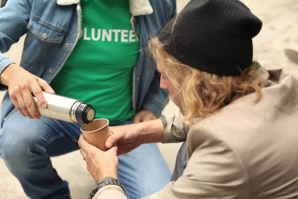 Voluntario dando de beber al hombre sin hogar al aire libre —  Fotos de Stock