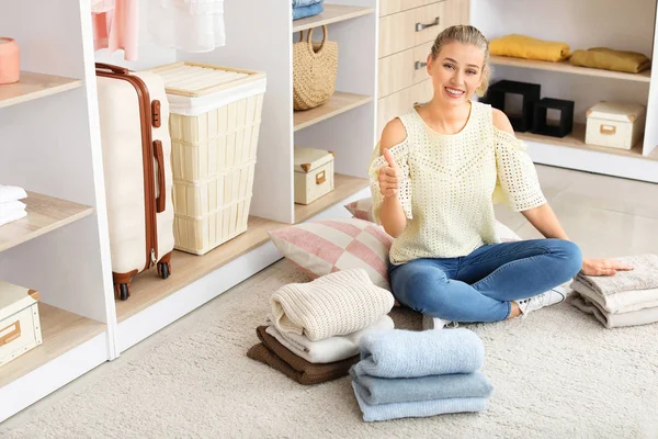Woman with stacks of clean clothes showing thumb-up gesture at home — Stock Photo, Image