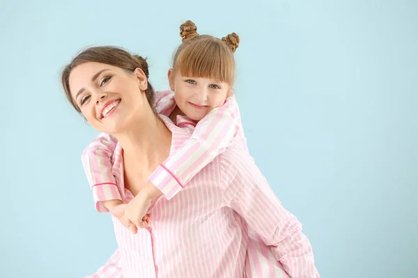 Portrait of happy mother and daughter in pajamas on color background — Stock Photo, Image