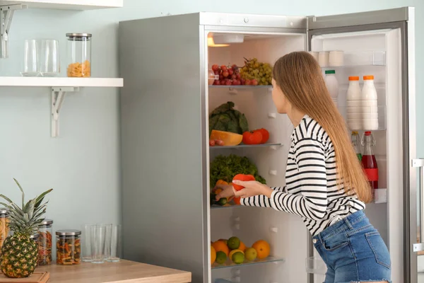 Frau holt zu Hause Lebensmittel aus dem Kühlschrank — Stockfoto