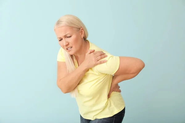 Mature woman suffering from back pain on color background — Stock Photo, Image