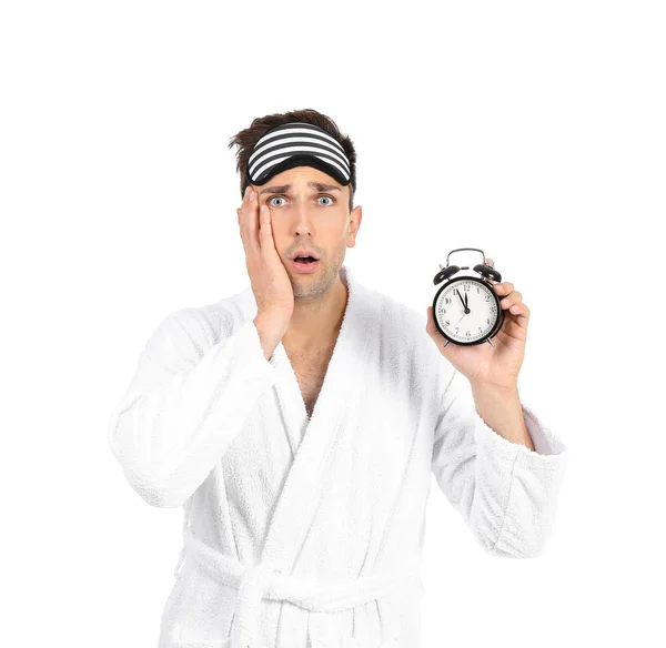 驚いた男でバスローブ、睡眠マスクと目覚まし時計で白い背景 — ストック写真