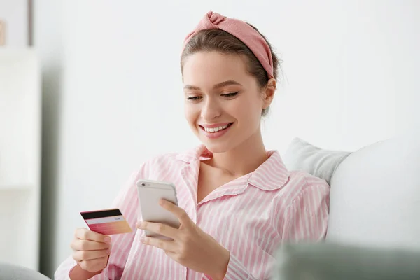 Jonge vrouw met creditcard en mobiele telefoon online winkelen thuis — Stockfoto