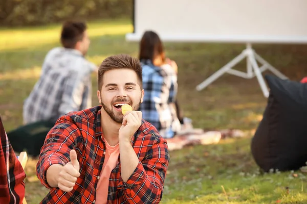Young man eating chips in outdoor cinema