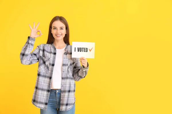 Молода жінка тримає папір з текстом I VOTED і показує добре на кольоровому фоні — стокове фото