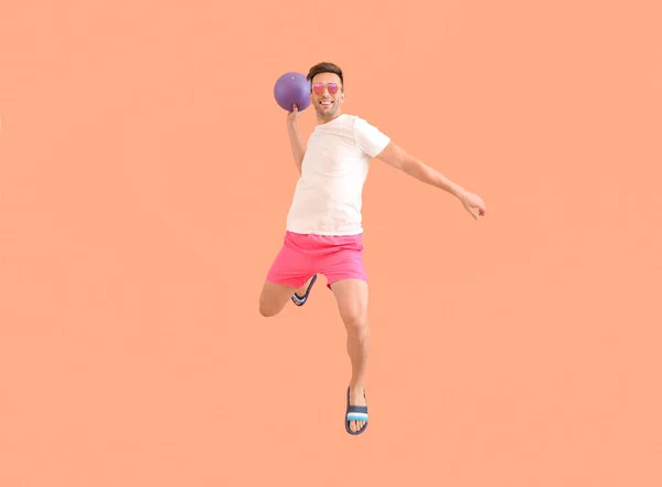 Прыгающий молодой человек с мячом на цветном фоне — стоковое фото