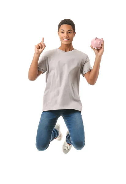 Saltando menino adolescente afro-americano com mealheiro e dedo indicador levantado no fundo branco — Fotografia de Stock