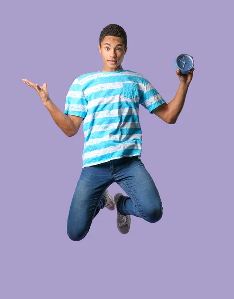 Jumping African-American teenager boy with clock on color background — ストック写真