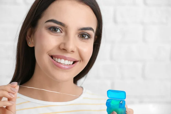 Beautiful young woman with dental floss on light background — Stock Photo, Image